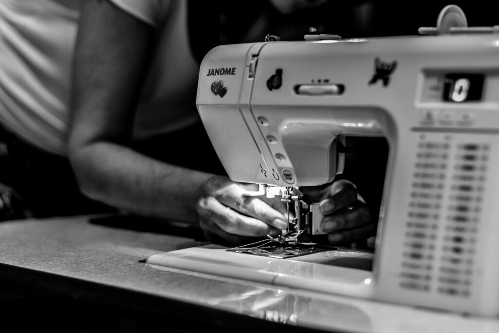 Detailed black and white photo of hands operating a sewing machine, showcasing craftsmanship.