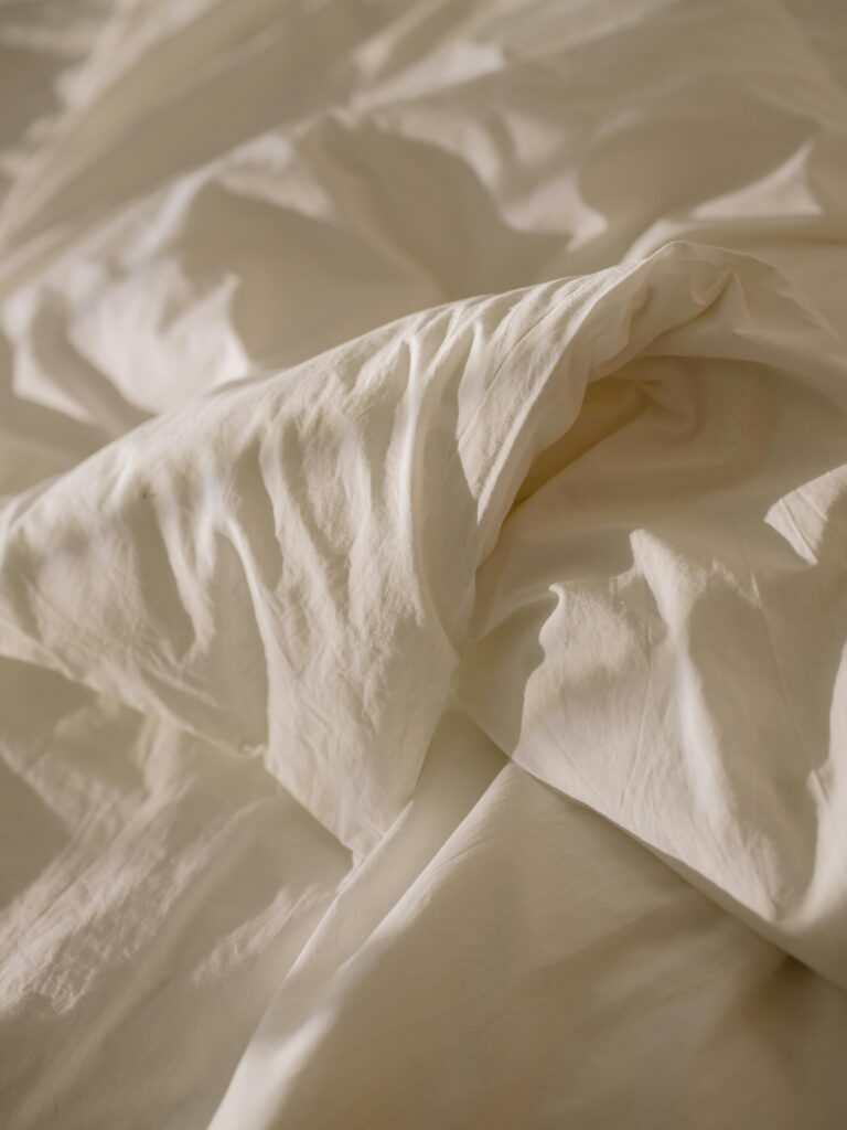 Close-up of crumpled white bed linen with soft natural lighting, evoking coziness.